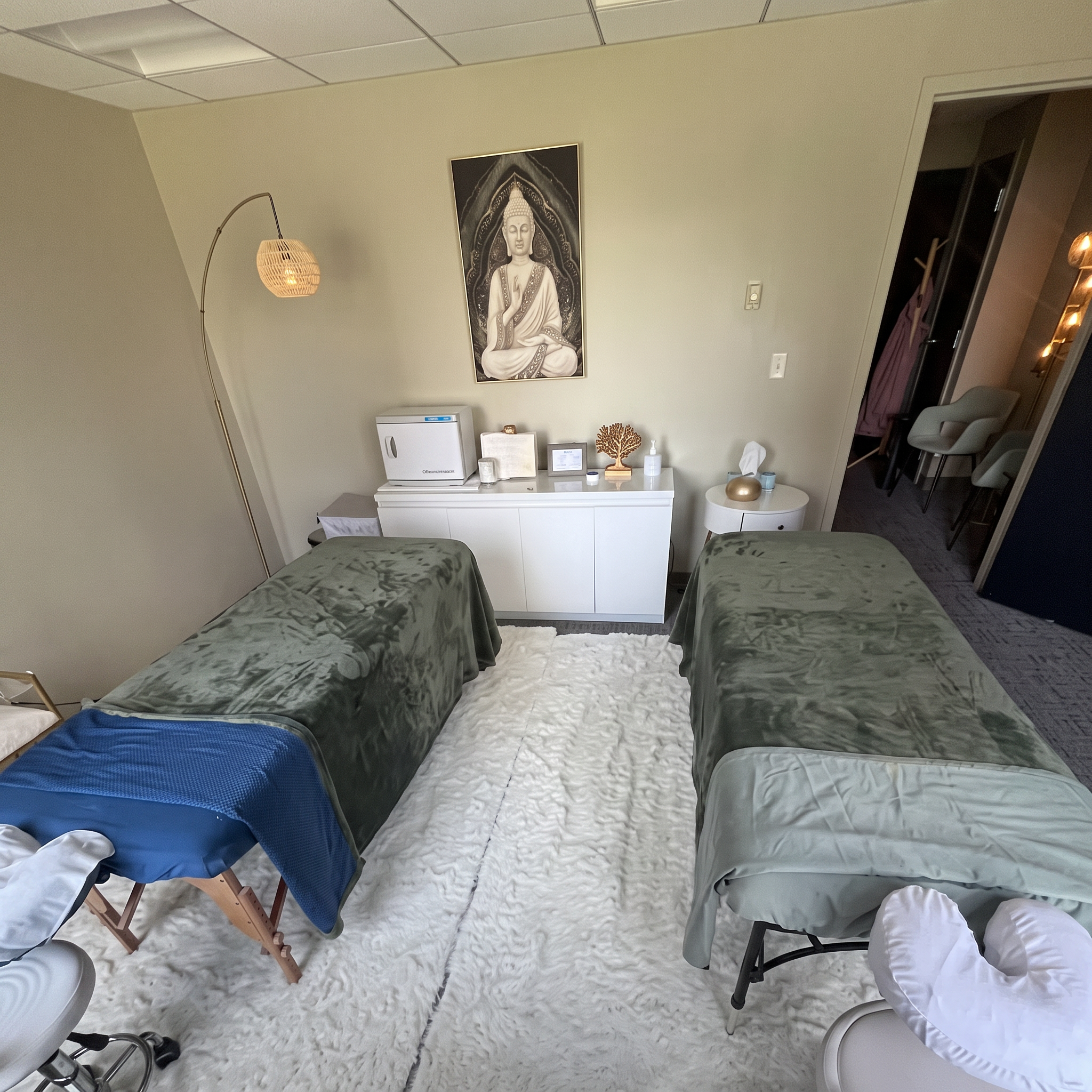 The couples room at Body Evolution Massage with two massage tables side by side, sage-green blankets and a Buddha print on the wall